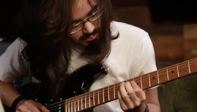 Mateus Asato, mit langen Haaren und Brille, spielt konzentriert auf seiner E-Gitarre.