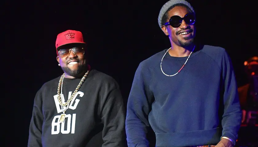 Die Mitglieder von Outkast, Big Boi mit roter Kappe und Andre 3000 mit grauer Mütze, lächeln auf der Bühne.