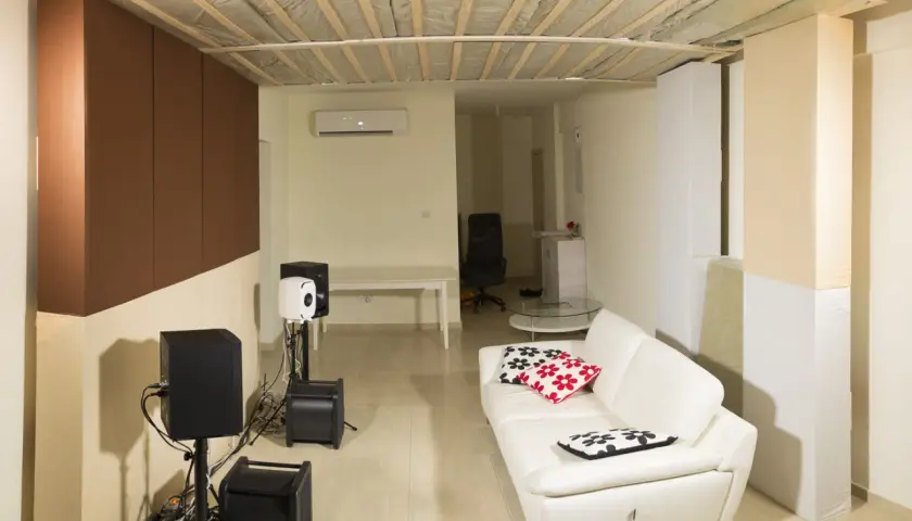 Ein Raum mit weißem Ledersofa, Lautsprechern und einer Deckenkonstruktion, die an ein **Deckensegel selber bauen** Projekt erinnert.