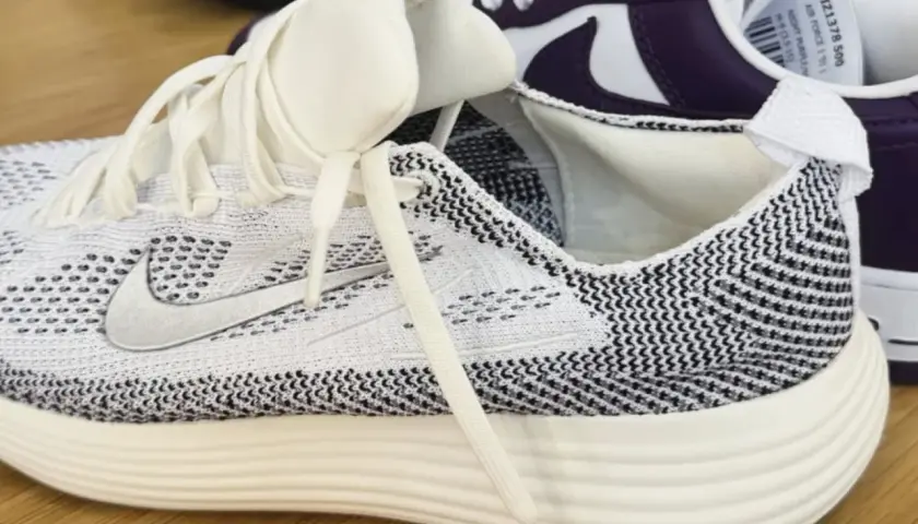 Weiße und schwarze **Shima Shima** Muster zieren diesen Laufschuh. Ein weiterer Schuh in Lila und Weiß ist im Hintergrund zu sehen.