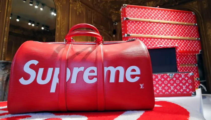 Rote Reisetasche mit weißem "Supreme"-Schriftzug und Louis Vuitton-Monogramm. Was ist Supreme? Luxus und Streetwear vereint.