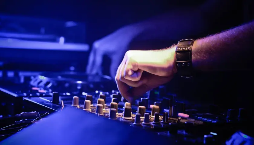 DJ-Hand mit Armband bedient Mischpult, um einen perfekten Mixtape zu erstellen. Blaue Beleuchtung.