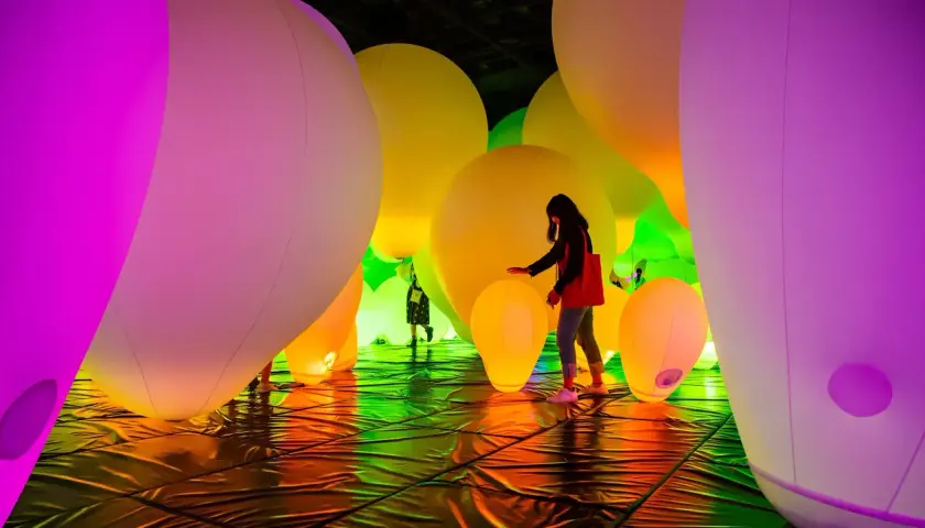 Menschen interagieren mit einer leuchtenden Installation aus riesigen, bunten Ballons. Ein immersives Kunsterlebnis.