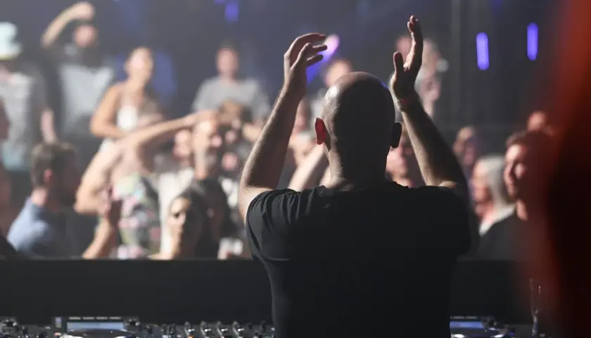 DJ mit erhobenen Armen vor jubelndem Publikum, der algoriddim djay-Controller im Vordergrund.