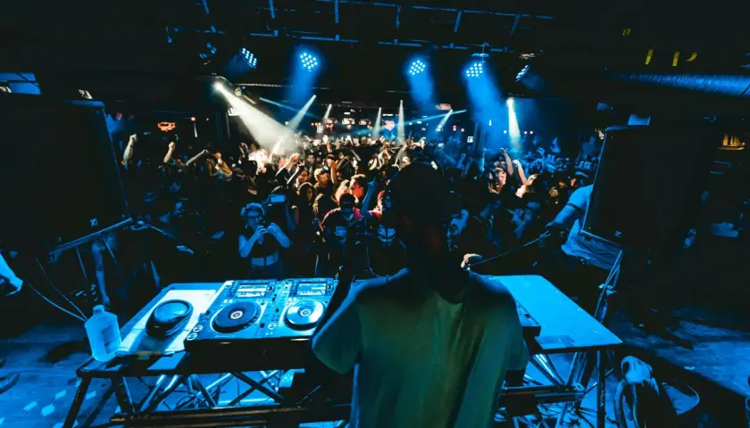 DJ legt auf, die Menge tanzt im blauen Licht. Die **DJ Musik** bringt alle zum Beben.