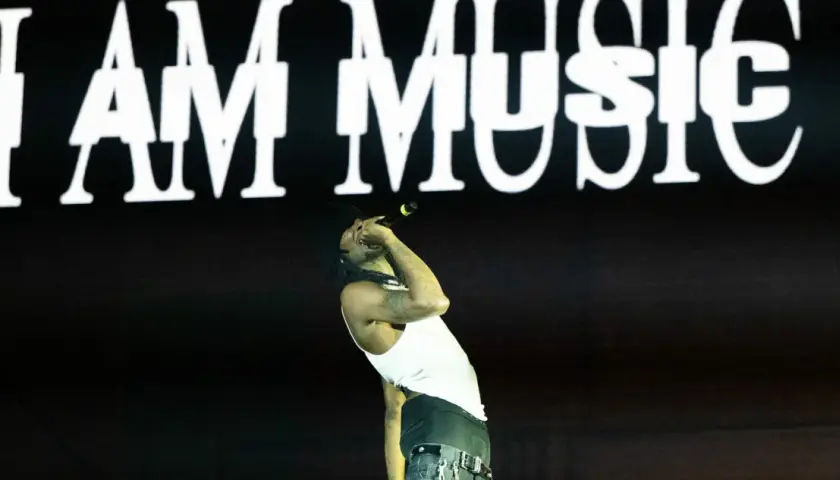 Ein Rapper singt vor einer Leinwand mit "I AM MUSIC" in weißer Schrift. Seine Performance ist pure art brut.