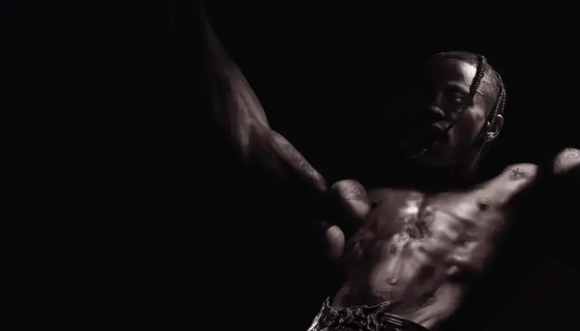 Travis Scott, mit tätowiertem Oberkörper, streckt die Arme aus und blickt intensiv in die Kamera. Ein Moment der rohen Energie, der an Travis' Utopia erinnert.