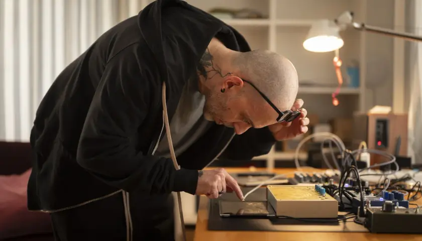 Mann mit Tattoos, der an einem Tisch mit elektronischen Geräten arbeitet, inspiriert von russischem Konstruktivismus.
