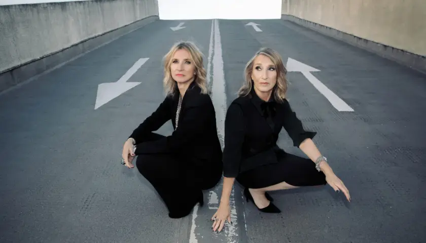 Susanne Freytag und ihre Partnerin, beide in eleganten schwarzen Outfits, hocken auf einer asphaltierten Rampe mit weißen Pfeilen.