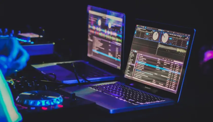 Zwei Laptops mit DJ-Software, beleuchtet von blauem und pinkem Licht, bereit für den nächsten Beat.