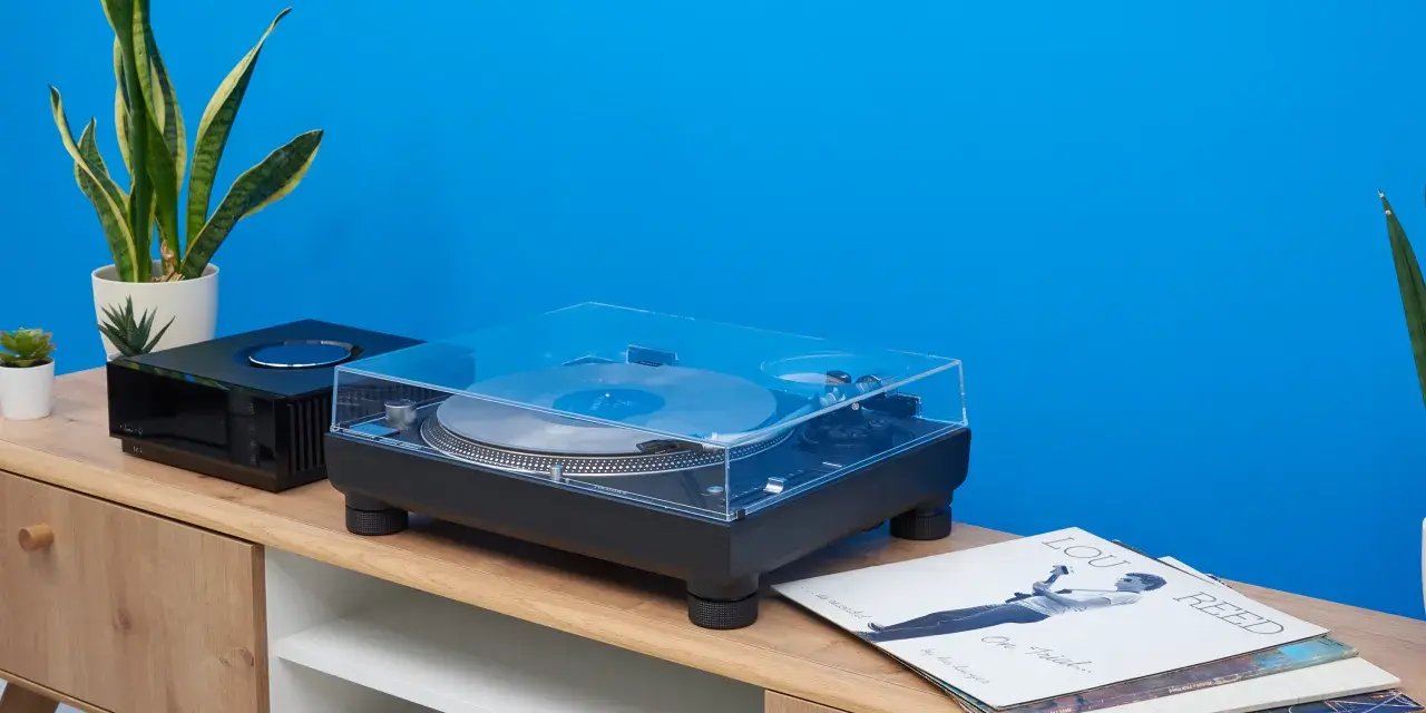 Technics SL-1210GR Plattenspieler mit Vinyl und Pflanzen auf einem Sideboard vor blauer Wand.