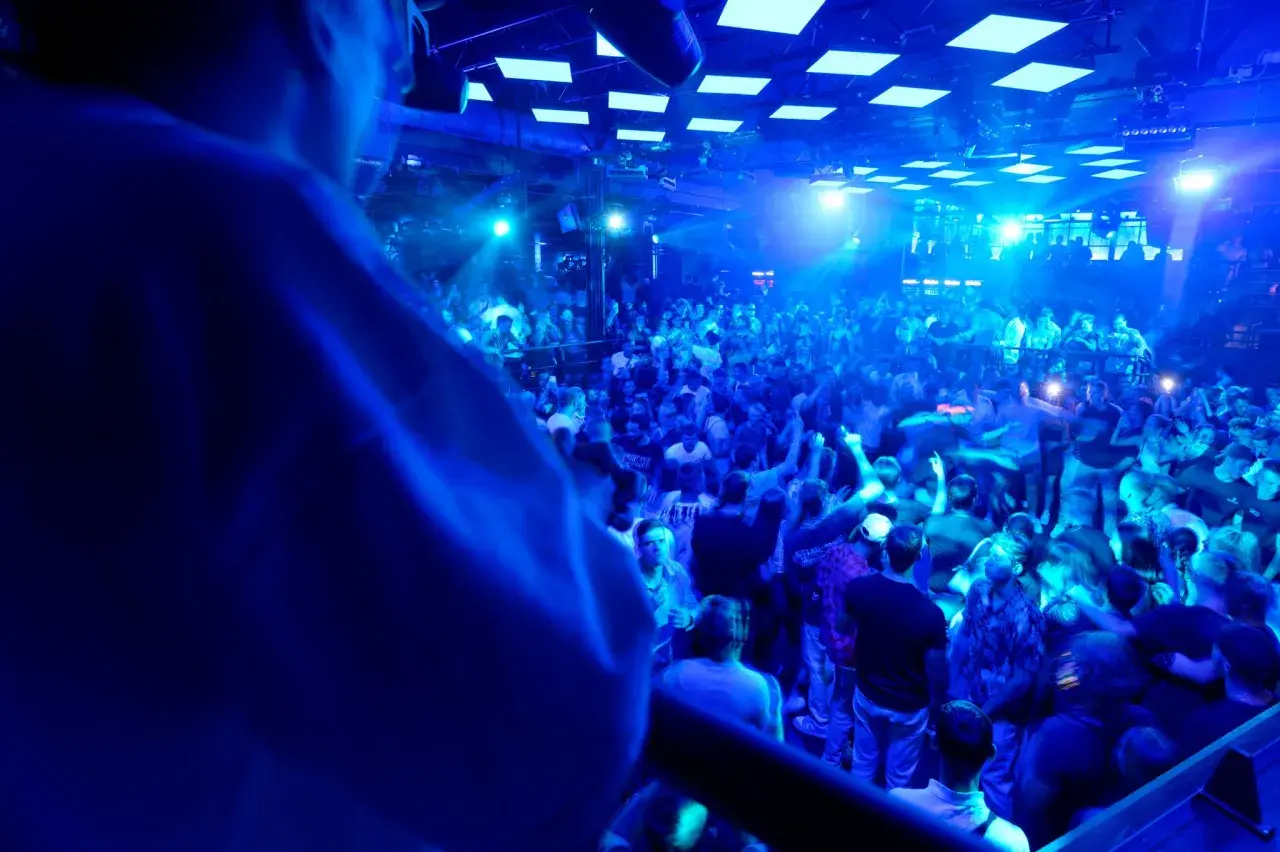 Eine Menge feiert zu den Klängen eines **live DJ** in einem Club. Blaue Lichter tauchen die Szene in eine pulsierende Atmosphäre.