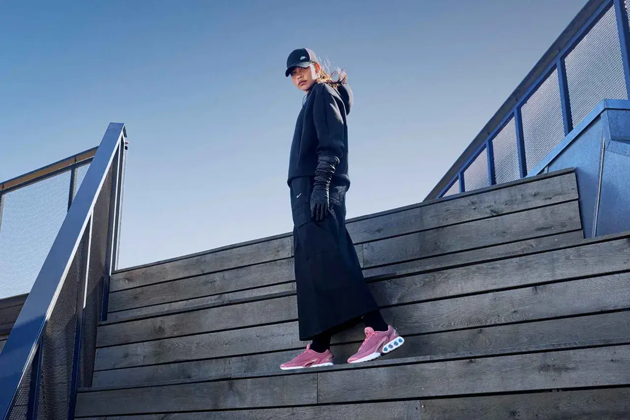 Frau in schwarzem Outfit und Nike Free Rush Schuhen auf Holztreppe.