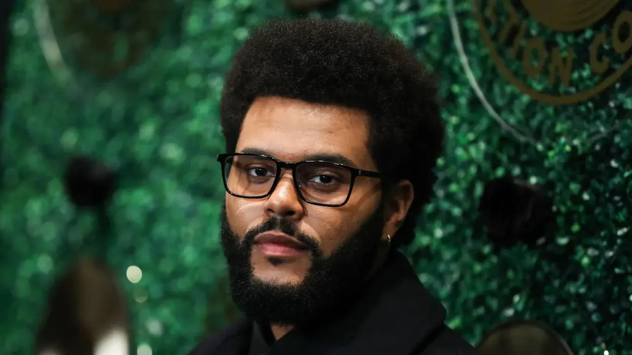 The Weeknd, mit Brille und Bart, posiert vor einer grünen Wand. Seine Musikkarriere begann in Toronto, Kanada.