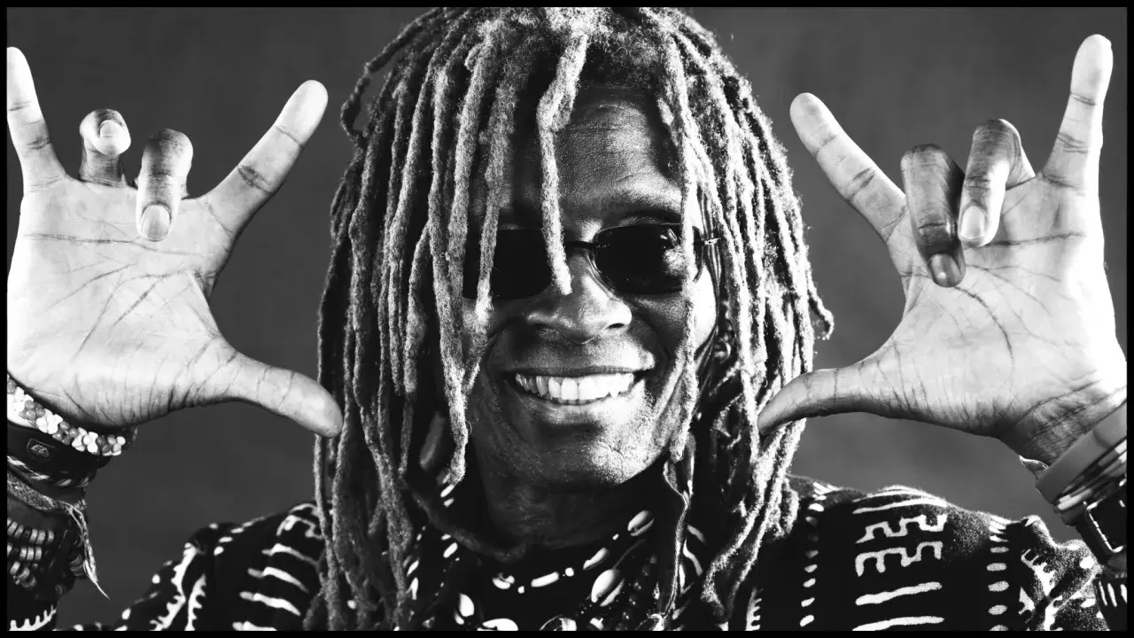 tm stevens mit Dreadlocks und Sonnenbrille, lächelnd und mit beiden Händen die "Rock on"-Geste zeigend.