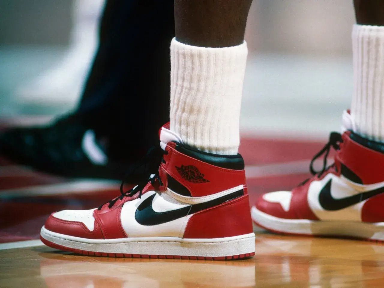 Ein Paar ikonische Air Jordan 1 Sneaker in Rot und Weiß, vielleicht der teuerste Schuh der Welt, auf einem Basketballplatz.