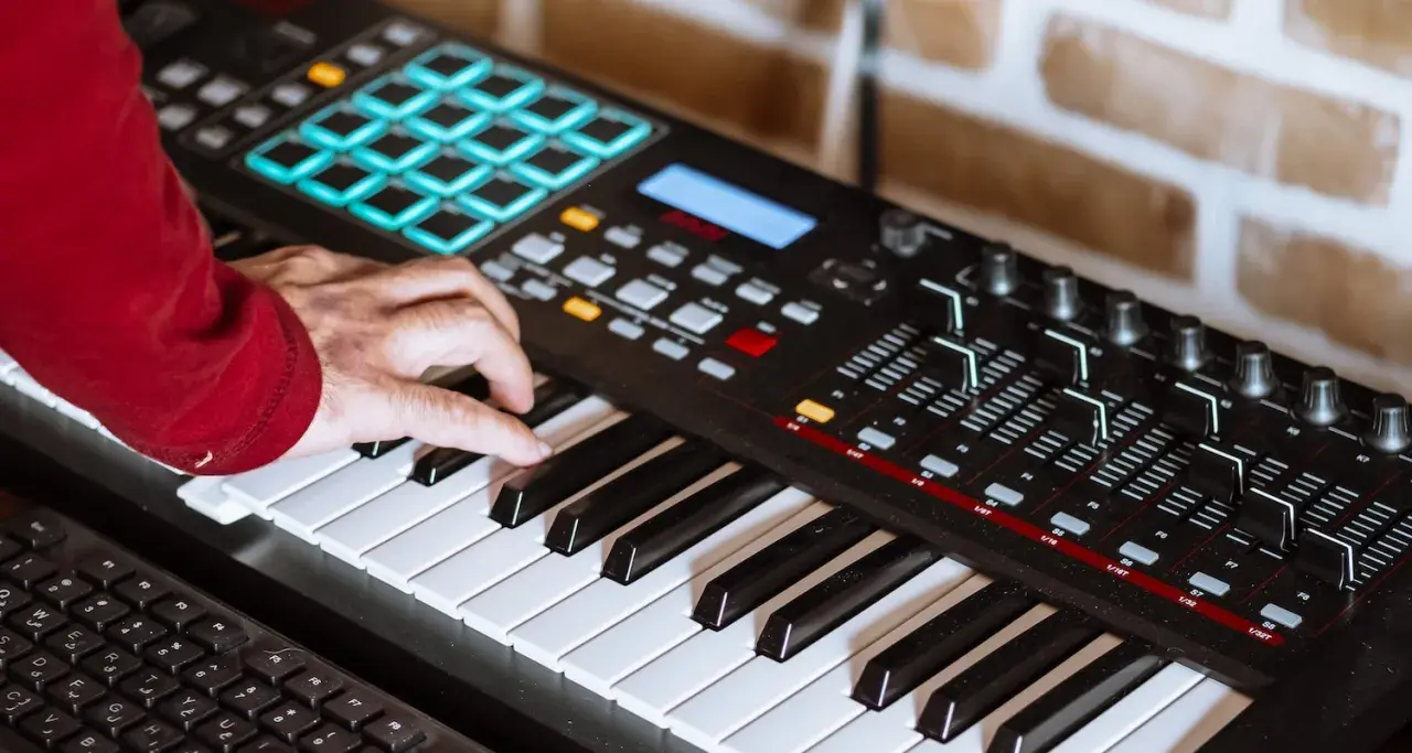 Hand spielt auf einem Keyboard, um Synthesizer-Musik zu kreieren. Bunte Pads und Regler sind sichtbar.
