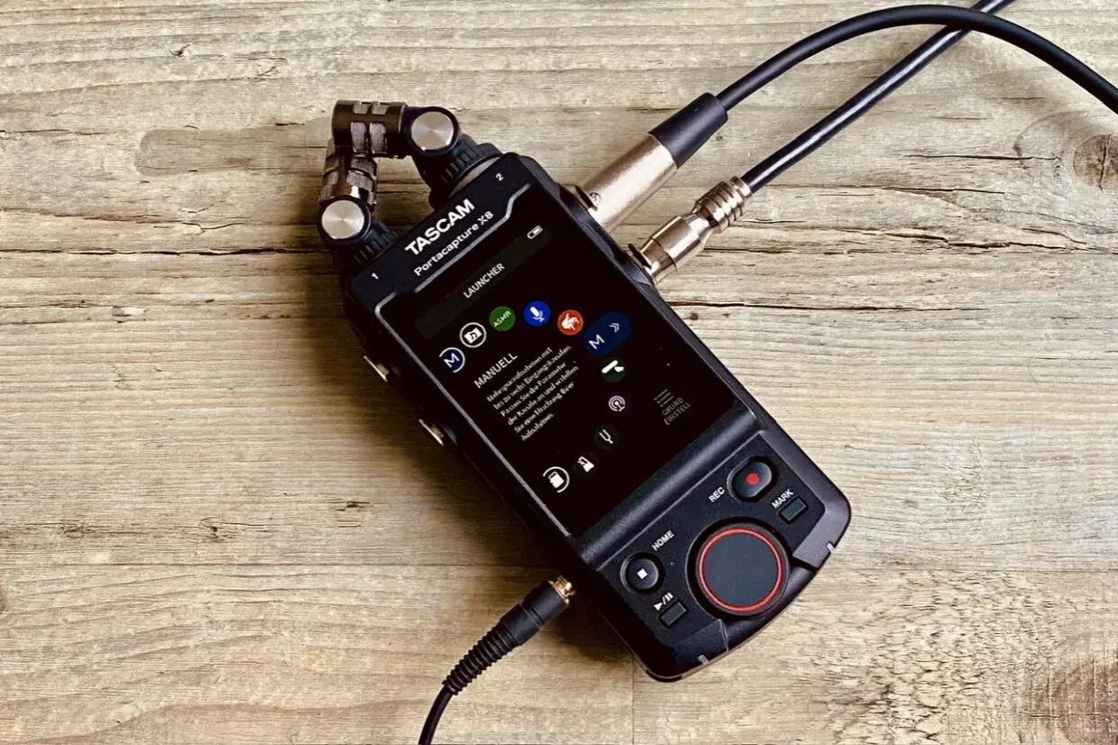 TASCAM Portacapture X8 mit angeschlossenen Mikrofonen auf Holzoberfläche. Ideal für Mehrspuraufnahmen.