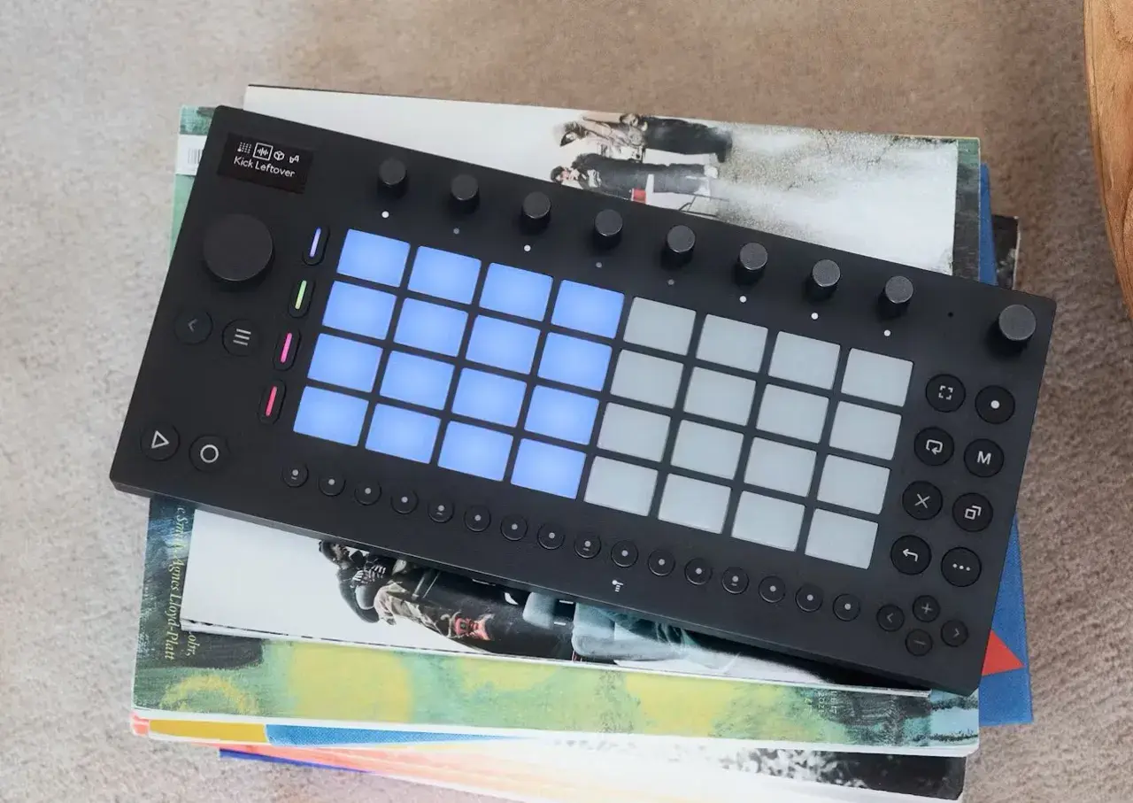 Ein schwarzes Ableton-Controller-Gerät mit leuchtenden blauen Pads liegt auf gestapelten Büchern.