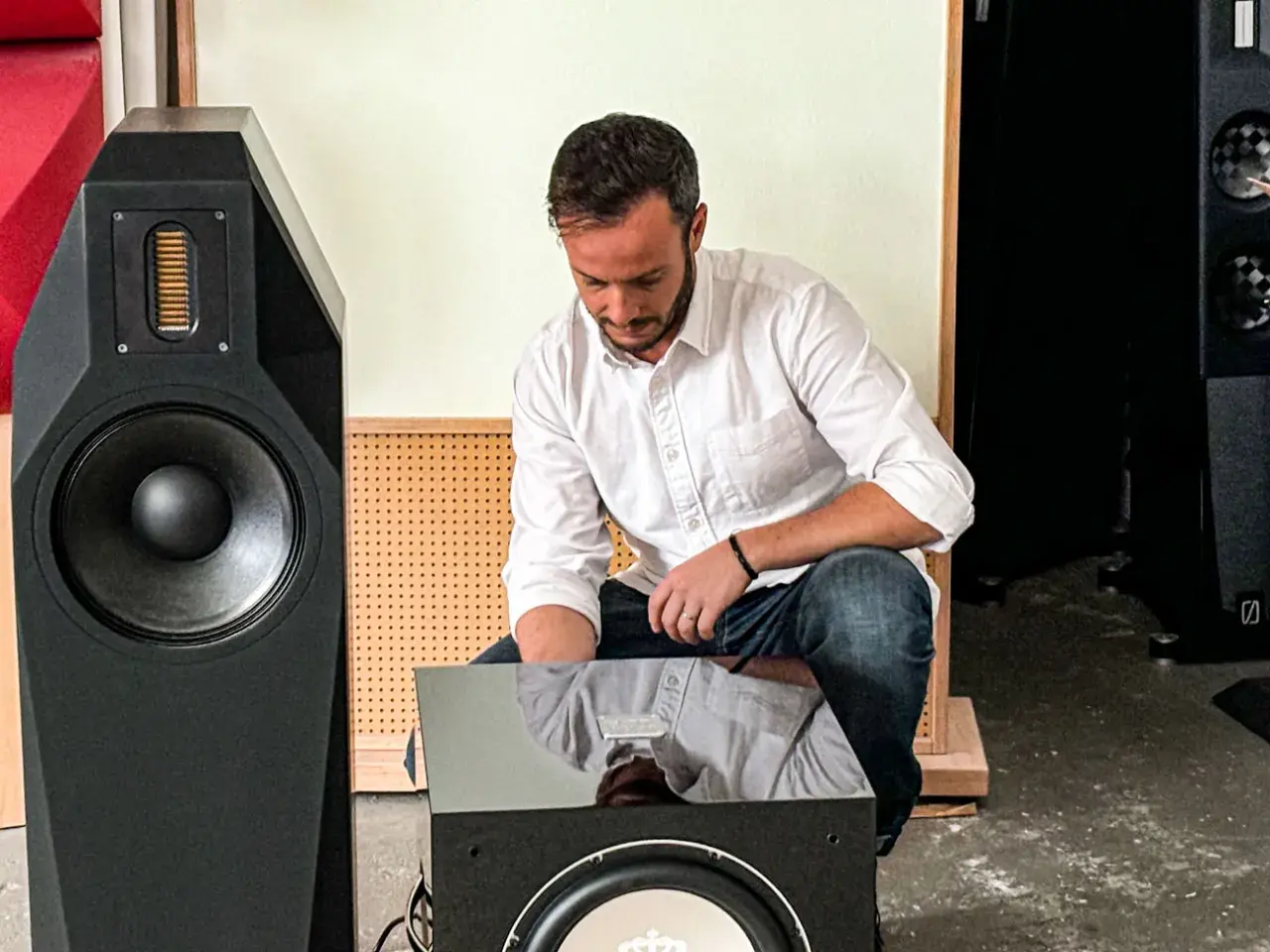 Mann im weißen Hemd und Jeans macht einen **subwoofer test** vor einem großen schwarzen Lautsprecher.