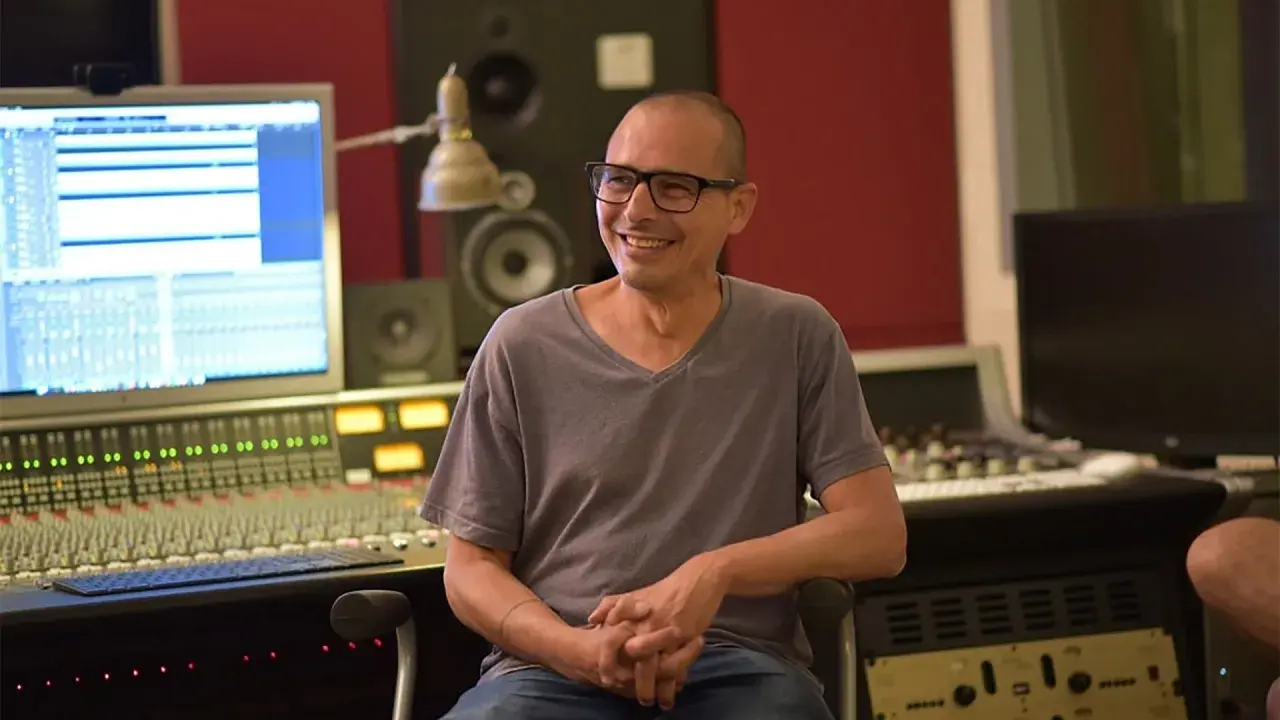 Moses Schneider, lächelnd in einem Tonstudio, sitzt vor einem Mischpult und einem Computerbildschirm.