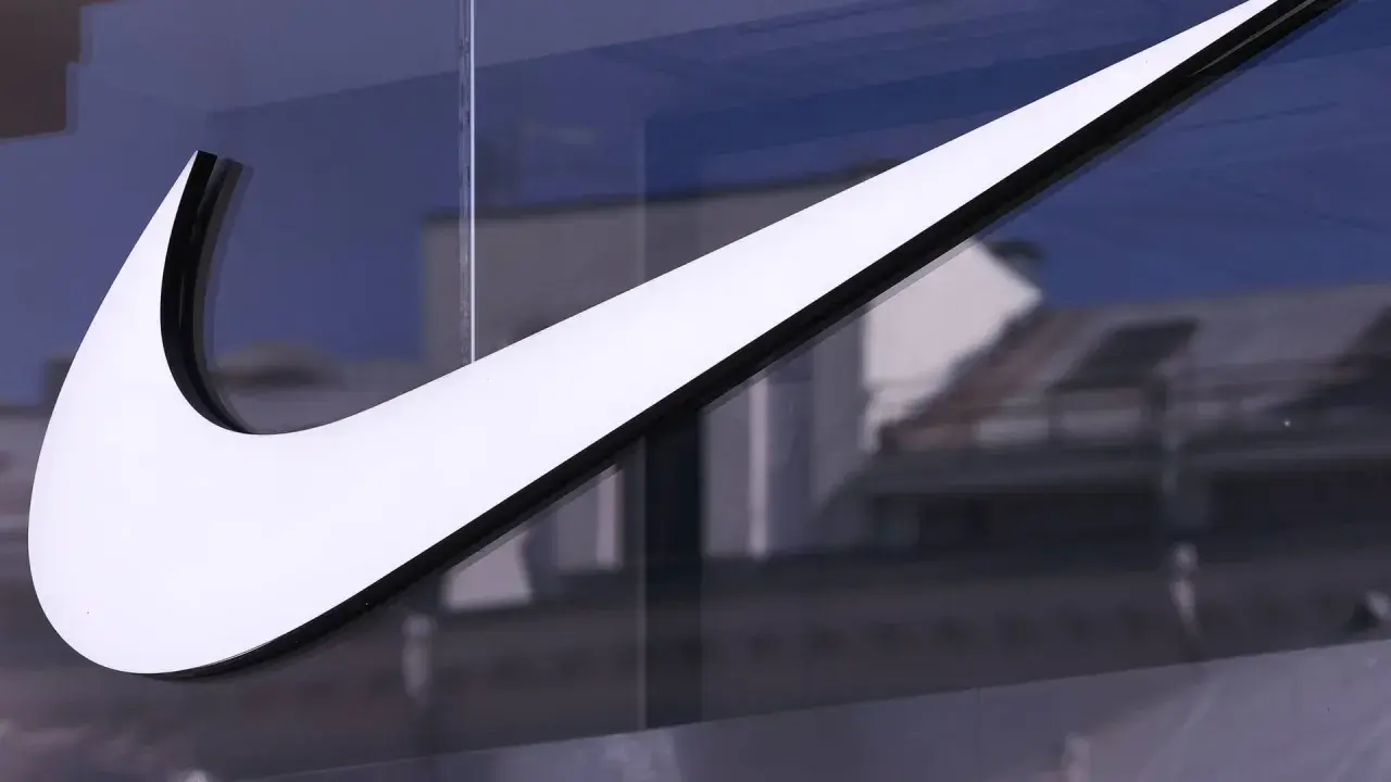 Das ikonische Nike-Logo, ein Symbol für die Nike Logo Entwicklung, leuchtet weiß vor einem blauen Himmel und reflektiert Gebäude.