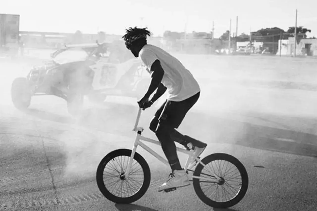 Nigel Sylvester fährt BMX, während im Hintergrund ein Buggy im Rauch steht.