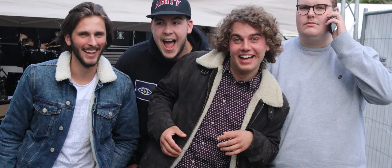 Vier junge Männer, die wie eine rap gruppe aussehen, lachen und posieren vor einer Bühne.