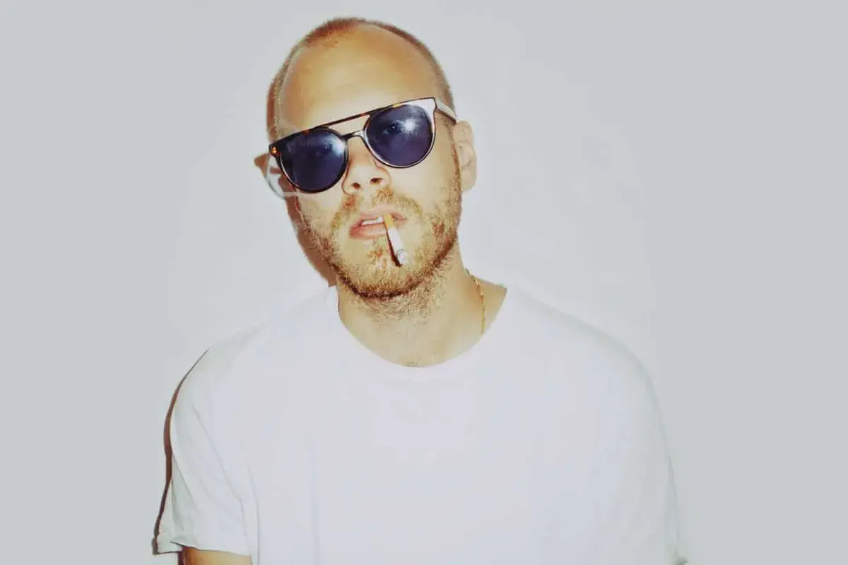 Phil Speiser, mit Sonnenbrille und Zigarette im Mund, trägt ein weißes T-Shirt.