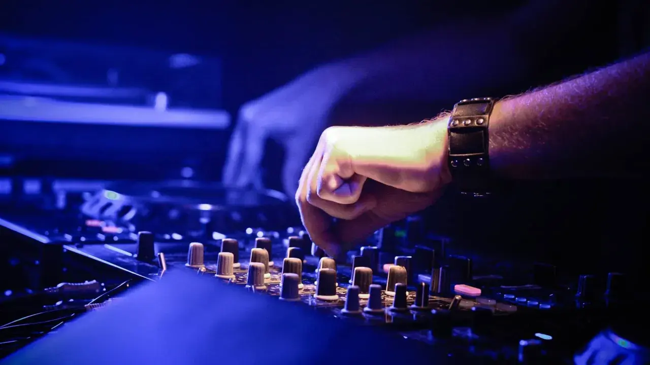 DJ-Hand mit Armband bedient Mischpult, um einen perfekten Mixtape zu erstellen. Blaue Beleuchtung.