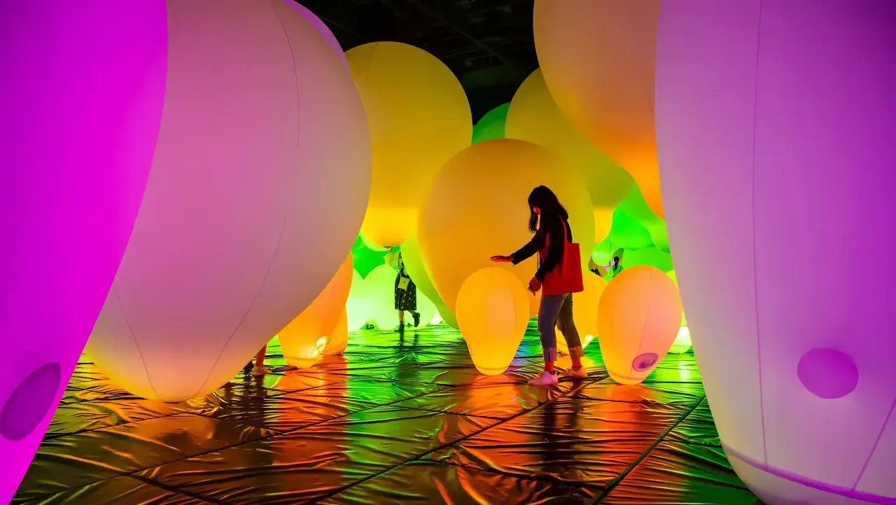 Menschen interagieren mit einer leuchtenden Installation aus riesigen, bunten Ballons. Ein immersives Kunsterlebnis.
