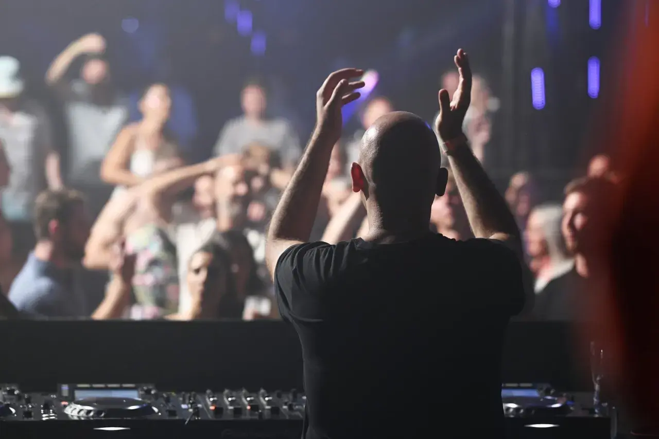DJ mit erhobenen Armen vor jubelndem Publikum, der algoriddim djay-Controller im Vordergrund.