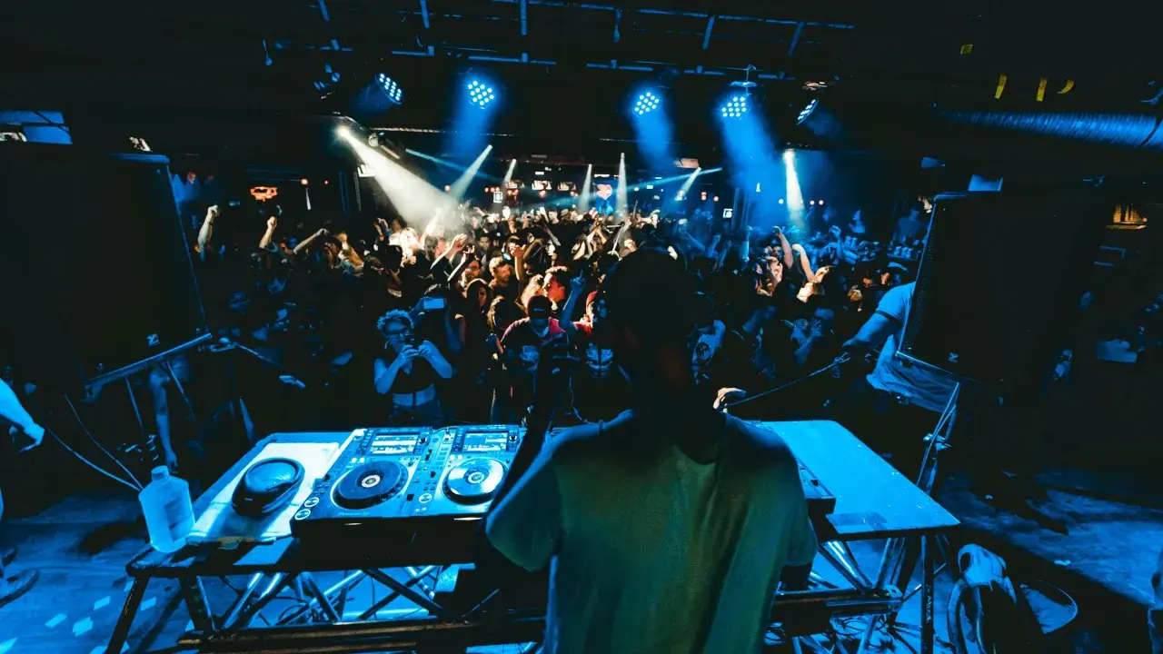 DJ legt auf, die Menge tanzt im blauen Licht. Die **DJ Musik** bringt alle zum Beben.