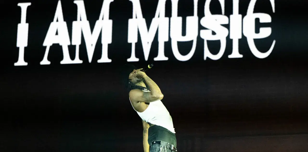 Ein Rapper singt vor einer Leinwand mit "I AM MUSIC" in weißer Schrift. Seine Performance ist pure art brut.
