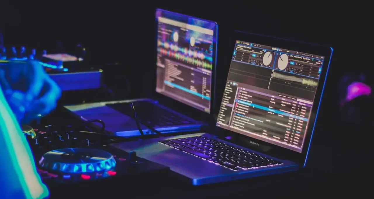 Zwei Laptops mit DJ-Software, beleuchtet von blauem und pinkem Licht, bereit für den nächsten Beat.