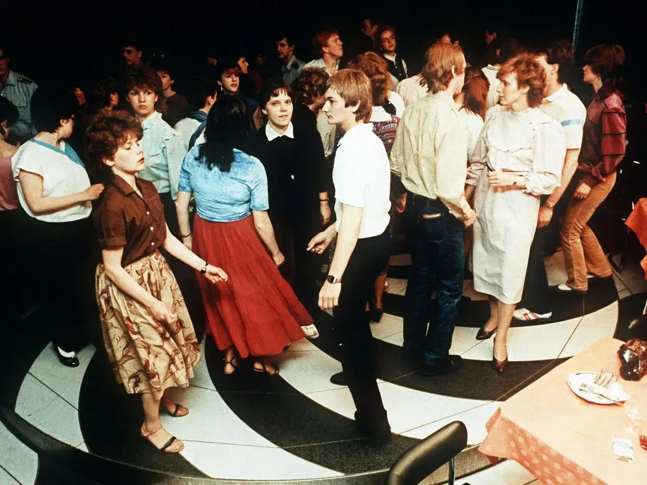 Junge Leute tanzen in einem Club der DDR. Ein DJ legt Musik auf, w&auml;hrend die Menge sich zur Musik bewegt.