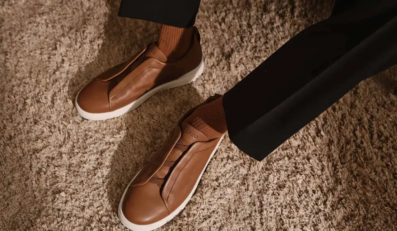 Elegante braune Leder-Sneaker mit wei&szlig;en Sohlen, getragen mit braunen Socken und schwarzen Hosen. Diese 1000 &euro; teuersten Schuhe der Welt strahlen Luxus aus.