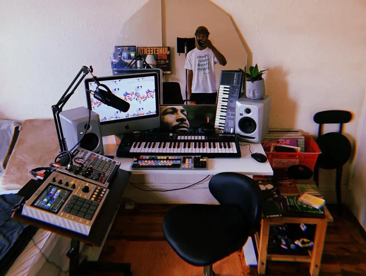Ein Mann im Spiegel reflektiert seine Musikproduktion. Ein Schreibtisch voller Keyboards, Mikrofone und MPCs – eine Art brutale, kreative Energie.