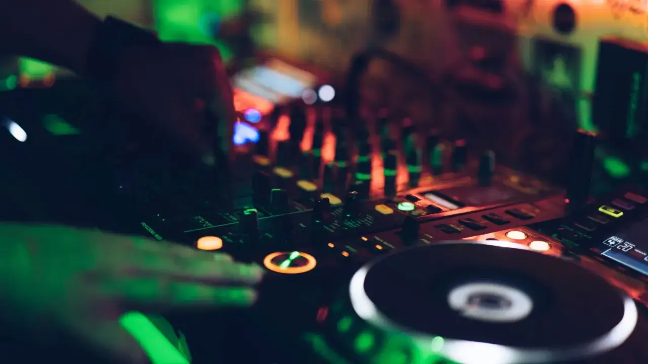 DJ-Hände bedienen einen Mixer, um einen perfekten Mixtape zu erstellen. Grüne und rote Lichter beleuchten die Szene.
