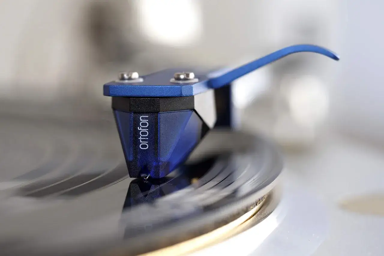 Nahaufnahme eines blauen Ortofon 2M Blue Tonabnehmers, der auf einer Vinylplatte f&uuml;r einen Test gleitet.