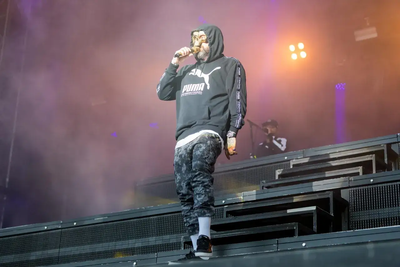 Rapper mit Totenkopfmaske und Puma-Hoodie auf B&uuml;hne. So sieht was ist rap aus: ein Mann, der seine Worte in die Menge schleudert.