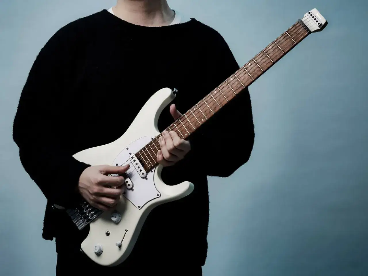 Eine Person in einem schwarzen Pullover spielt eine wei&szlig;e E-Gitarre. Die Finger von Ichika Nito bewegen sich geschickt &uuml;ber das Griffbrett.