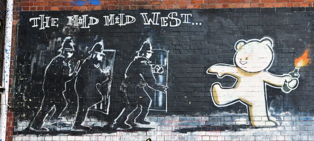 Ein Teddyb&auml;r mit Molotowcocktail steht vor Polizisten. Ein Werk, das an Banksy erinnert, fragt: 