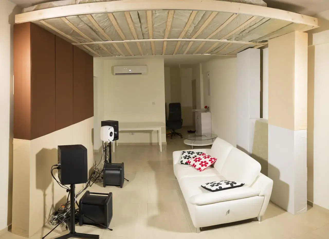 Ein Raum mit wei&szlig;em Ledersofa, Lautsprechern und einer Deckenkonstruktion, die zeigt, wie man ein Deckensegel selber bauen kann.