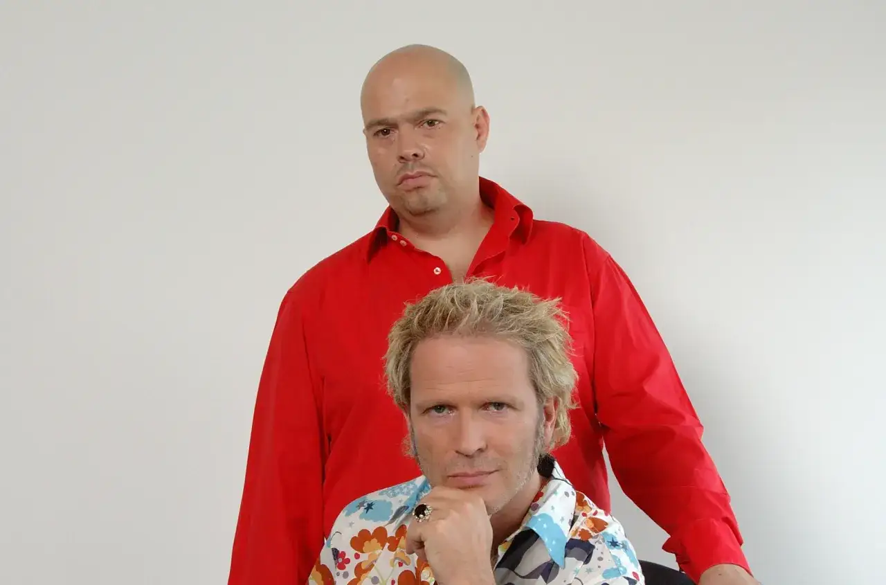Zwei M&auml;nner, einer mit Glatze und rotem Hemd, der andere mit blonden Haaren und buntem Hemd, posieren f&uuml;r ein Foto. Sie sind jam el mar.