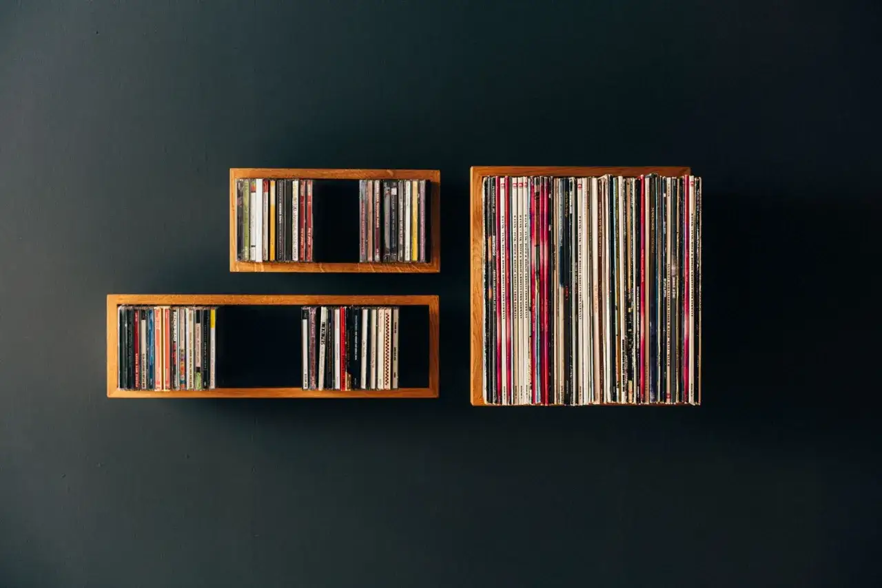 Drei Holzregale an einer dunklen Wand, gef&uuml;llt mit vielen bunten Schallplatten.