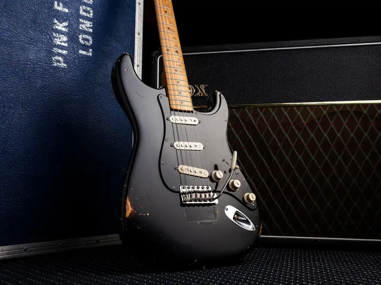 Eine abgenutzte schwarze E-Gitarre, die teuerste Gitarre der Welt, steht neben einem Verst&auml;rker und einem Koffer mit der Aufschrift 