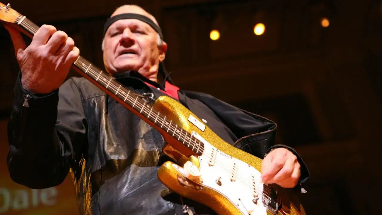 Dick Dale, der Surf-Rock-Pionier, spielt seine goldene E-Gitarre mit einem Stirnband.