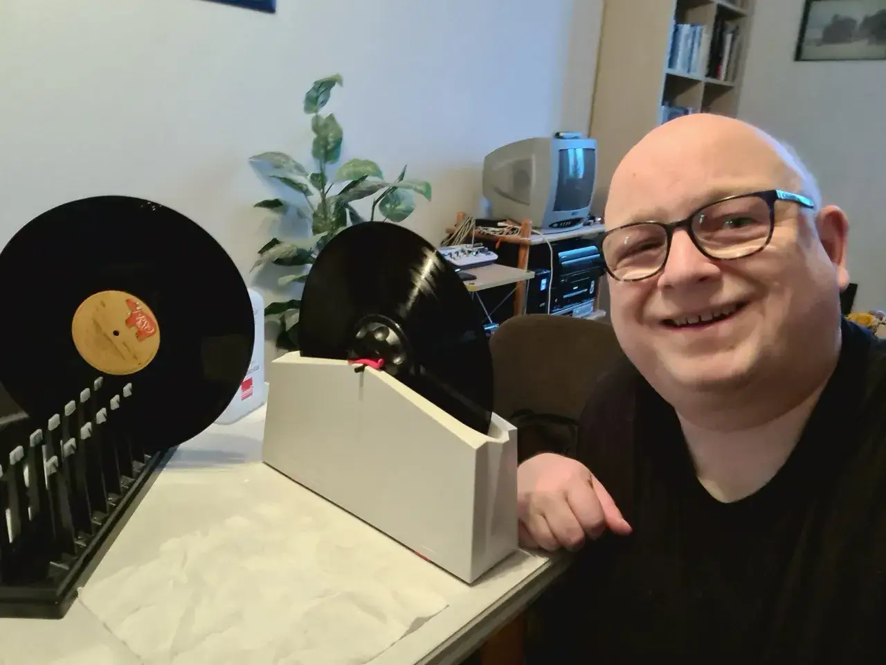 Mann l&auml;chelt, w&auml;hrend er seine Schallplatten w&auml;scht. Eine Schallplatte steht in einer Halterung, eine weitere liegt daneben.