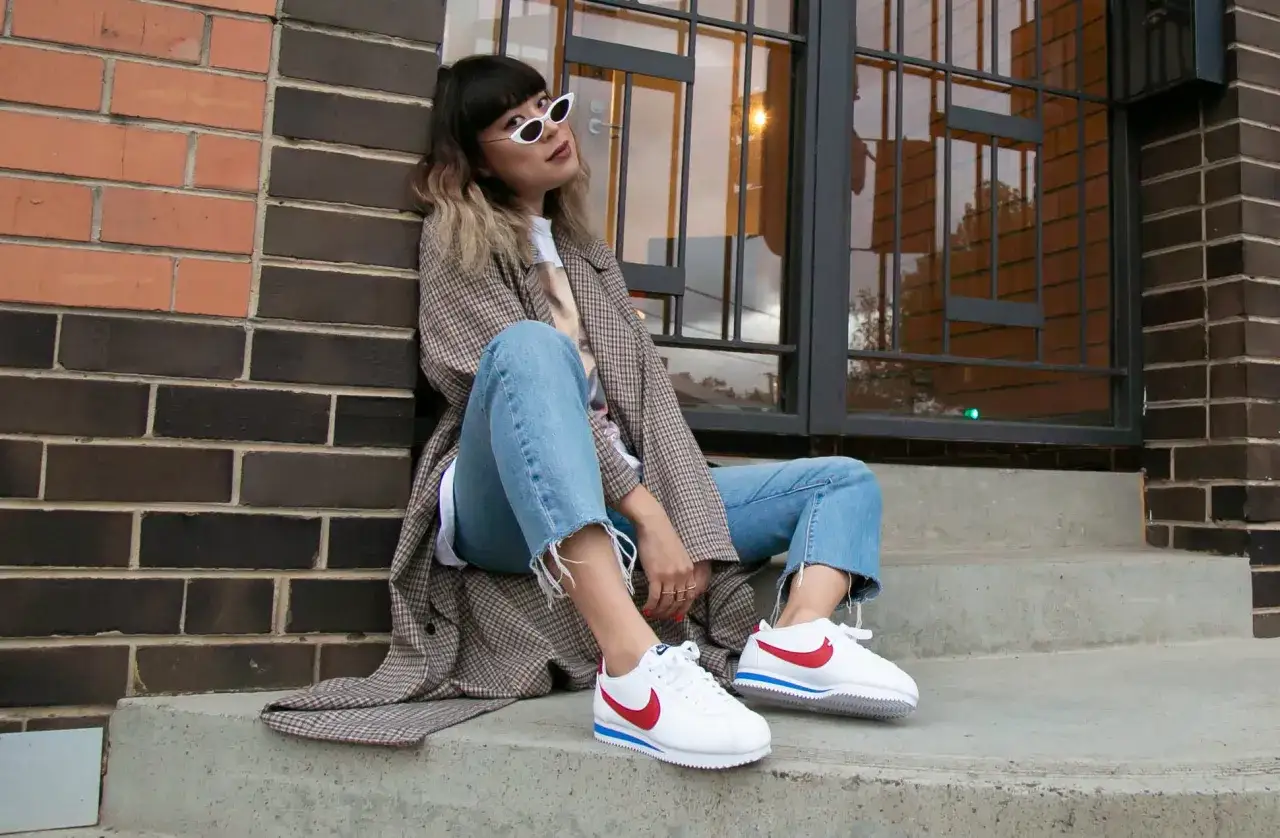 Frau in Jeans und kariertem Mantel tr&auml;gt wei&szlig;e Nike Cortez, den ersten Nike Schuh von 1972.